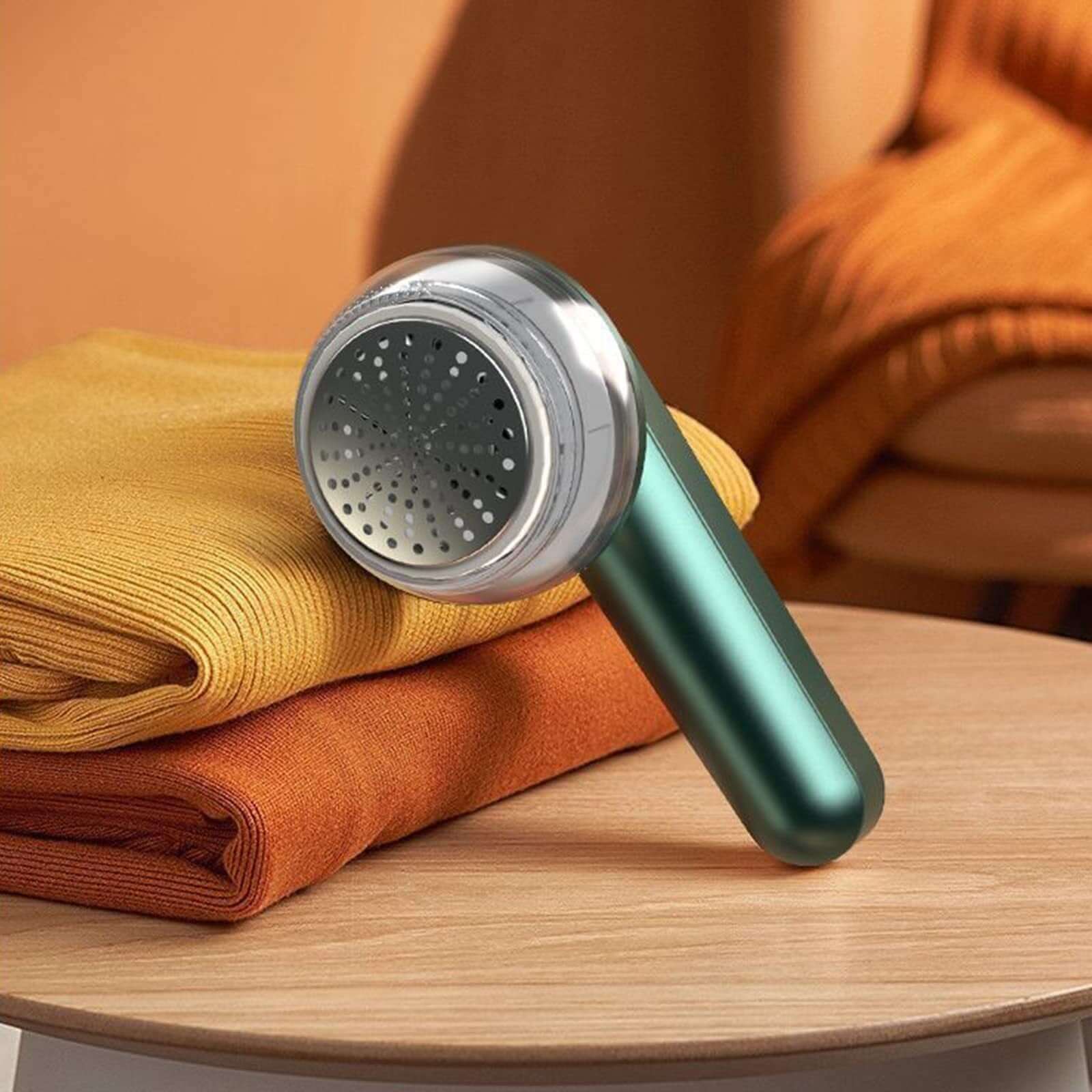 USB Electric Lint Remover on a table with folded sweaters in vibrant colors.