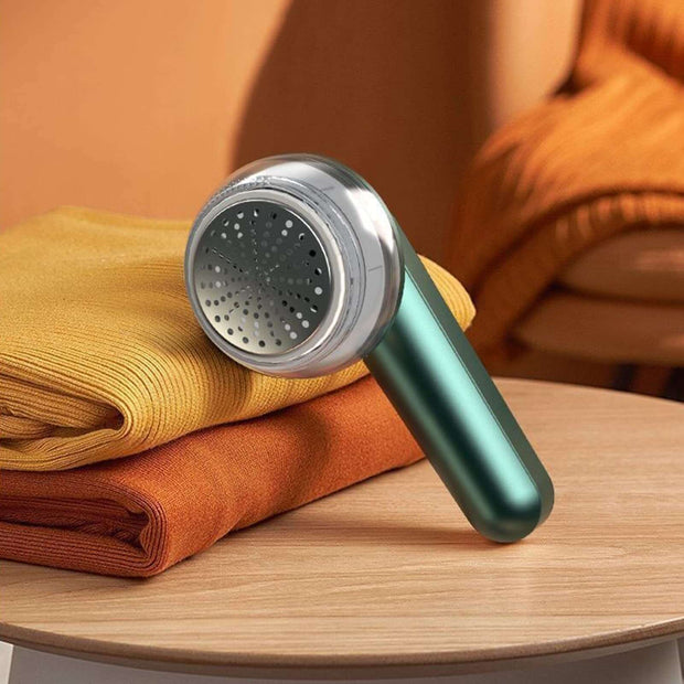 USB Electric Lint Remover on a table with folded sweaters in vibrant colors.